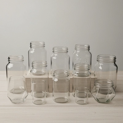 A collection of various styles of empty glass jars suitable for candle making, arranged neatly on a wooden surface.